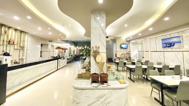 A modern hotel lobby with a marble reception desk, seating area, and a central column with decorative items. - Grand Malioboro Yogyakarta Hotel (Gedong Tengen)