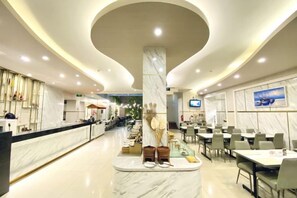 Un hall d’hôtel doté d’un comptoir de réception en marbre, d’un espace salon et d’une colonne centrale agrémentée d’éléments décoratifs.