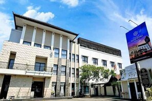A multi-story building with a prominent entrance, large windows, and a clear sky. - Grand Malioboro Yogyakarta Hotel (Gedong Tengen)