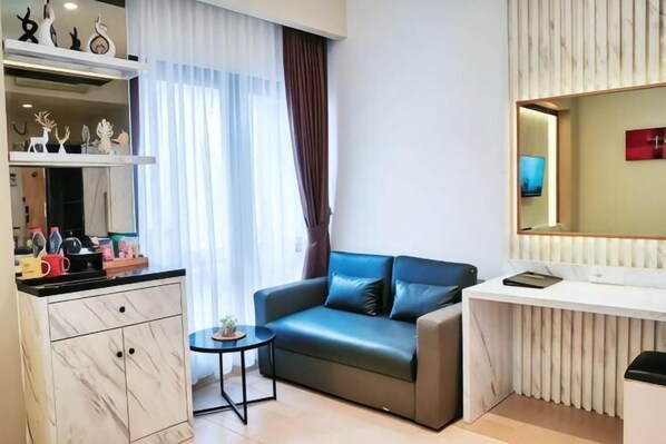 A modern living room with a sofa, a small table, a desk, and a large mirror. - Grand Malioboro Yogyakarta Hotel (Gedong Tengen)