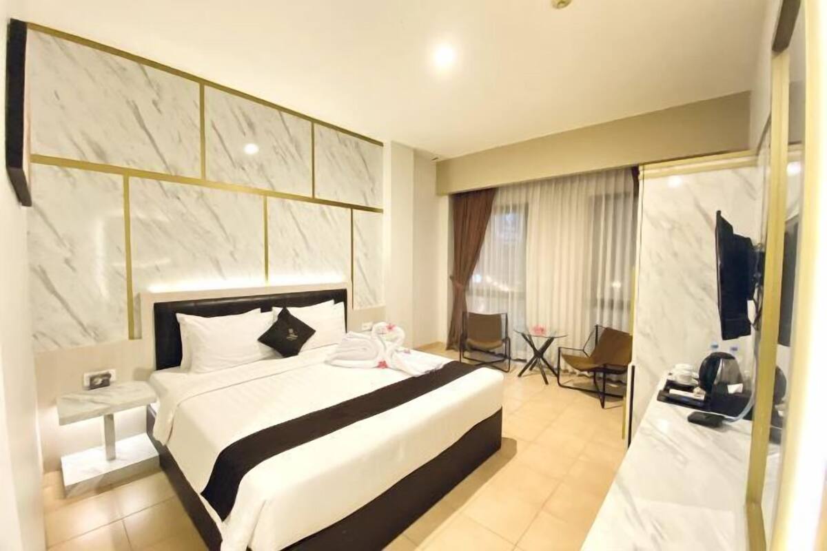 Ein Hotelzimmer mit einem großen Bett, einem Nachttisch, einem Sessel, einem kleinen Tisch und einem Spiegel.