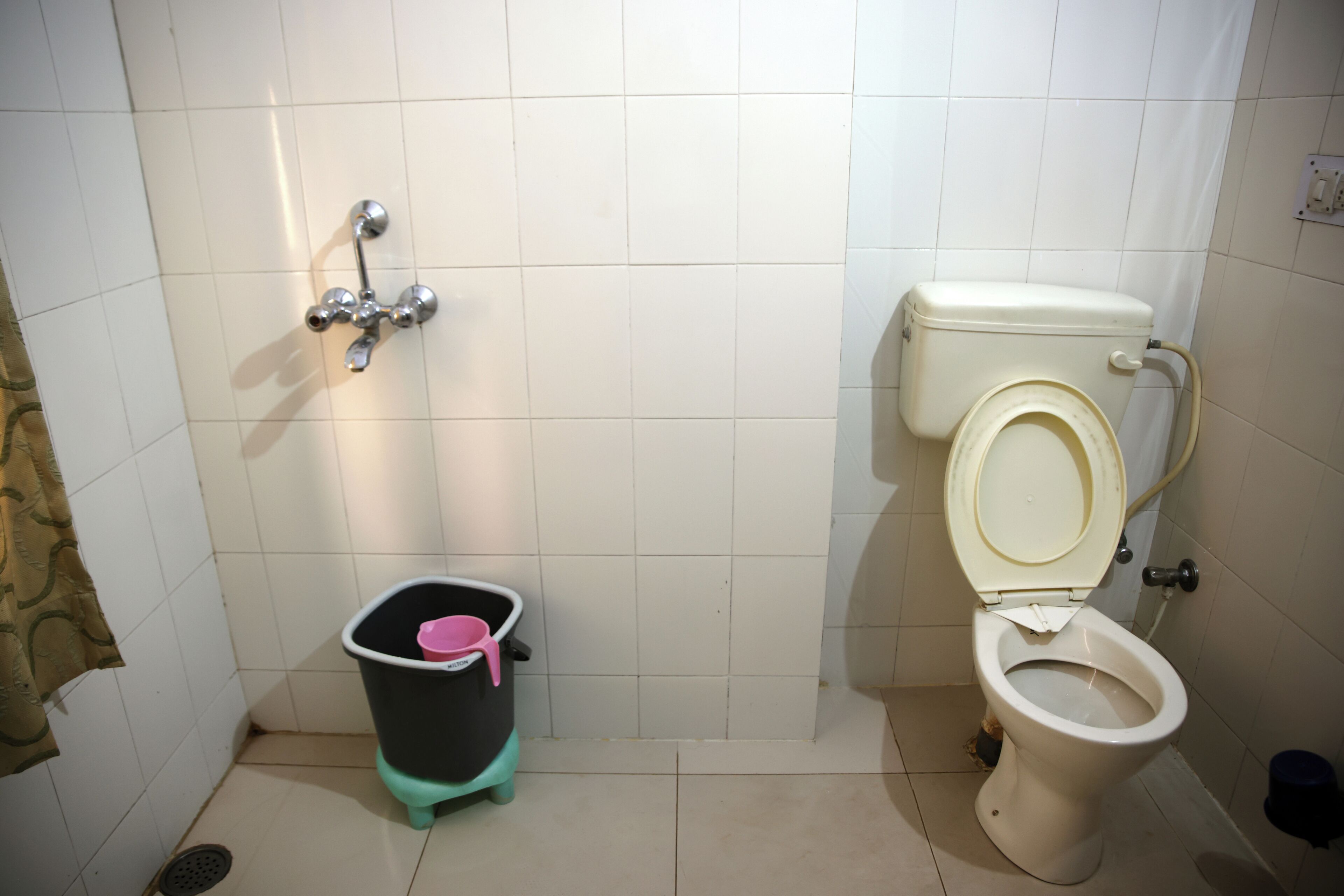 A small bathroom with a toilet, a shower, and a trash bin.