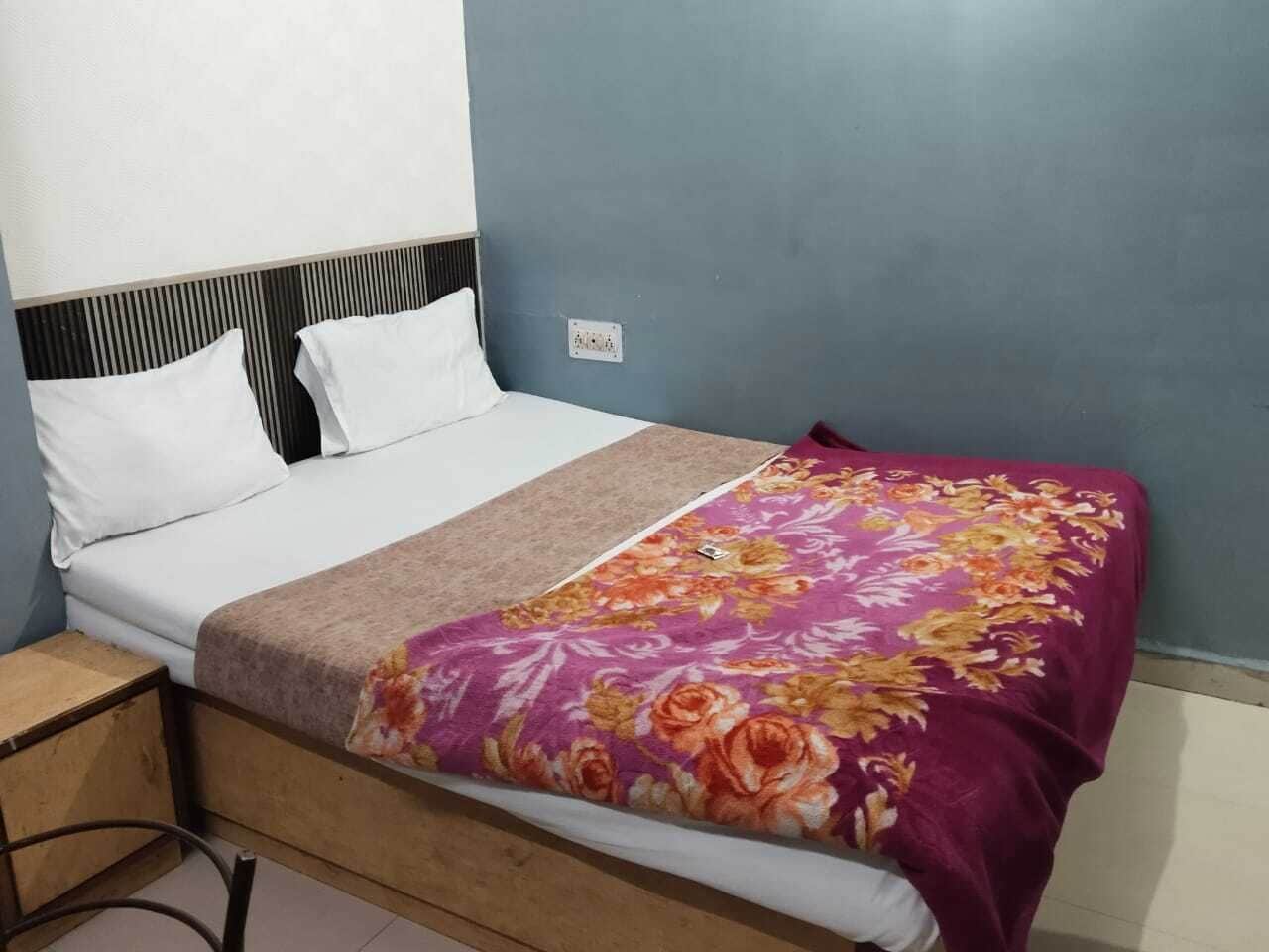 A single bed with a white mattress, a floral-patterned blanket, and a headboard with vertical slats.