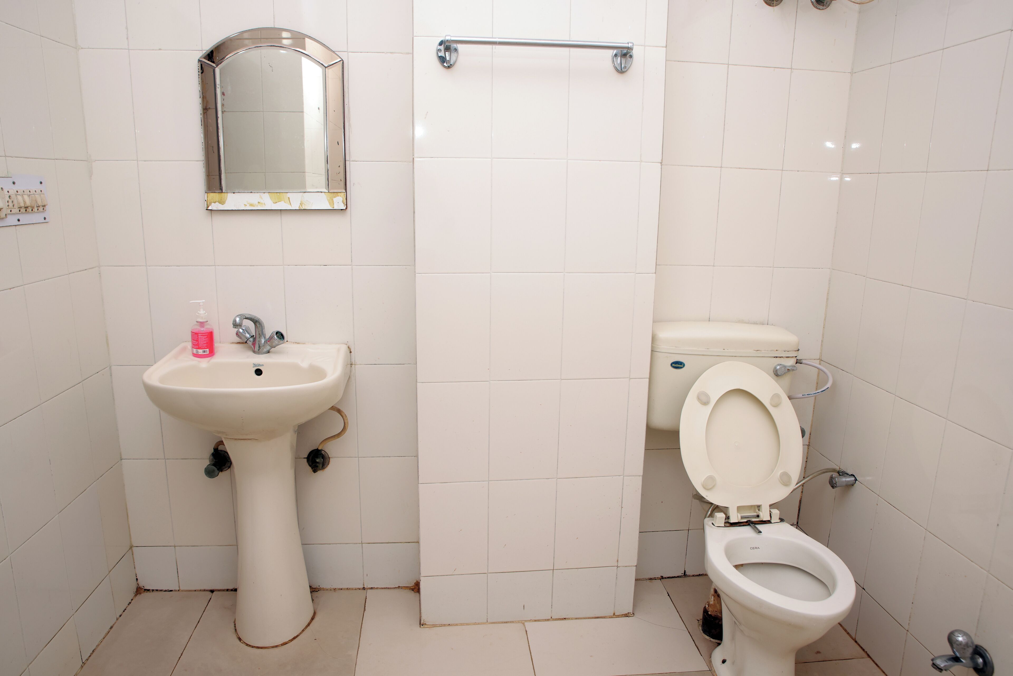 Casa de banho com lavatório de pedestal, espelho, sanita e dispensador de gel desinfetante.
