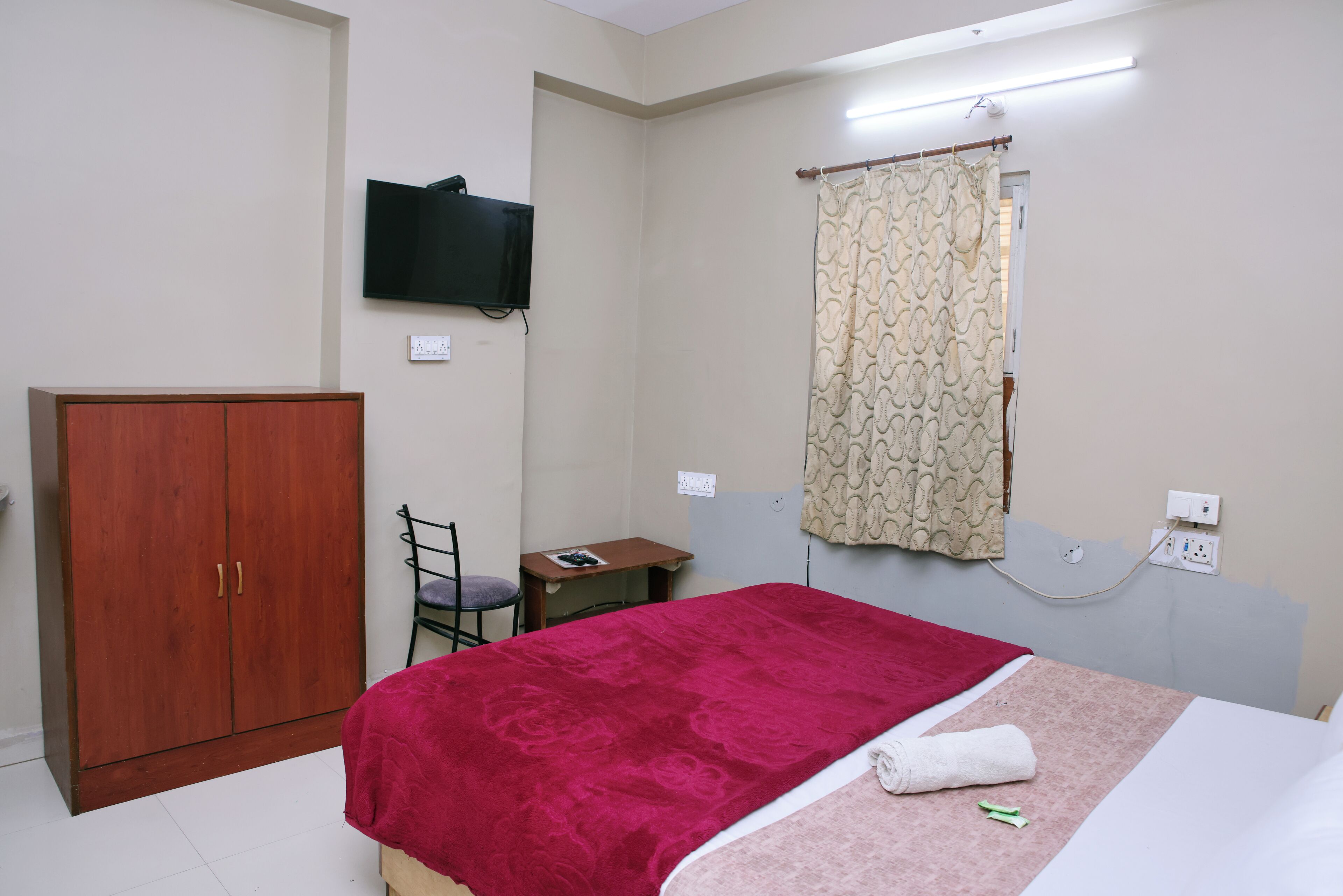 Une chambre à coucher comprenant un lit, une armoire, un bureau, une chaise, un téléviseur et un rideau.