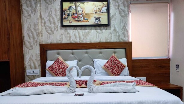A neatly made bed with a white bedspread, two red patterned pillows, and two swans made of towels.