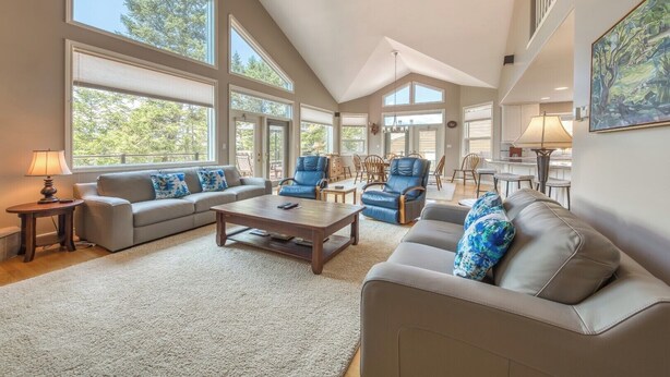A spacious living room with large windows, a high ceiling, and a dining area.