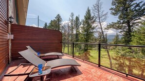 A balcony with two lounge chairs and a small table, overlooking a forested area with a view of distant mountains.