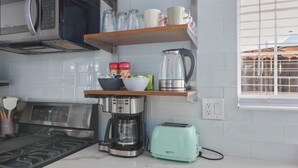 Une cuisine équipée d’un four à micro-ondes, d’une machine à café, d’un grille-pain et de divers ustensiles de cuisine rangés sur des étagères.