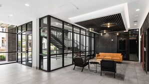 A modern lobby with glass walls, a staircase, and a seating area with a sofa and chairs. - Chic Music Row Condo - Pool, Rooftop Deck with City View, Gym, Office + More! (Nashville)