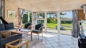 A spacious living area with a wooden ceiling, large windows offering a view of a green landscape, a sofa, chairs, and a coffee table.