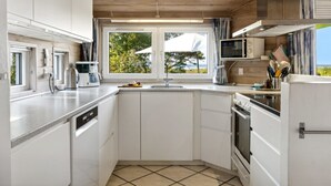 A compact kitchen with white cabinets, a built-in oven, a microwave, and a window with a view of greenery.
