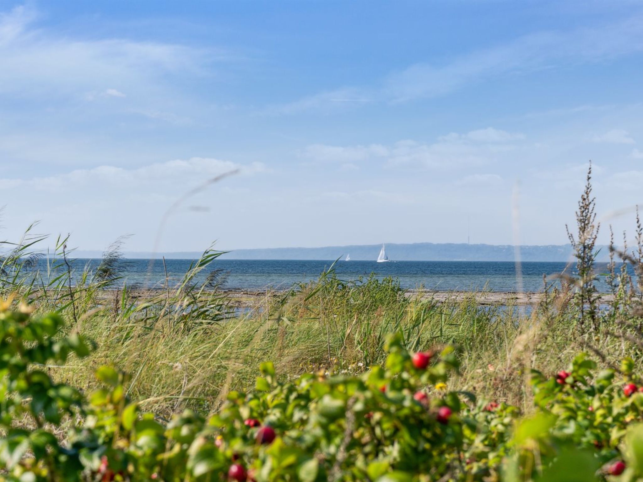 Een kustlandschap met uitzicht op zee en verre zeilboten.