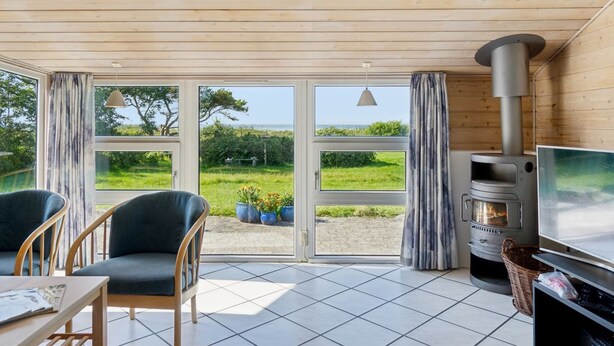A cozy room with a wooden ceiling, large windows, a fireplace, and a television.