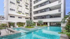 Ein modernes Hotel mit einem zentral gelegenen Schwimmbad, mehreren Balkonen und üppiger Bepflanzung.