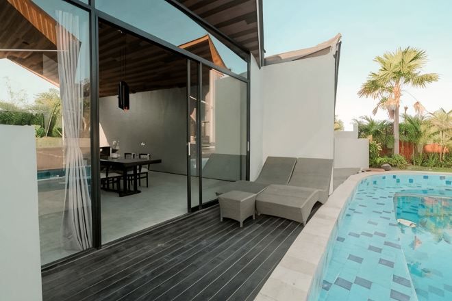 A modern outdoor pool area with a glass enclosure, a wooden deck, and a seating area.
