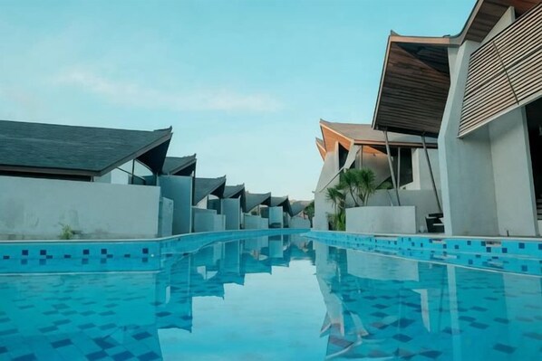 Una piscina con borde de azulejos, rodeada de edificios modernos con techos planos y un cielo despejado.
