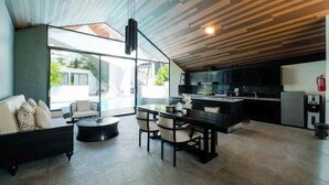 A modern living space with a dining area, kitchen, and large glass doors leading to an outdoor area. - The Lavana Akatara Villa Nusa Dua (Bali)