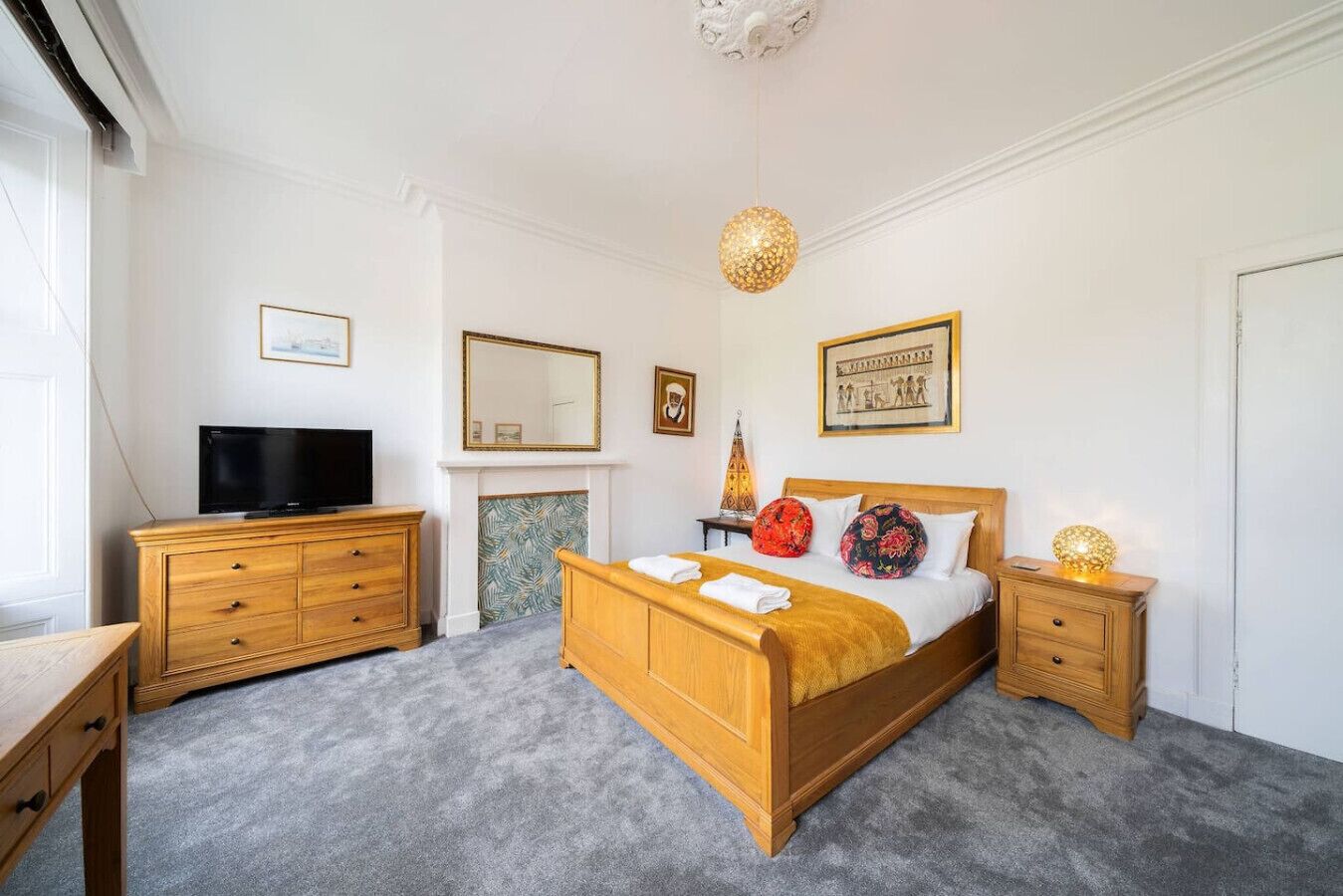 Un dormitorio con cama de madera, televisor sobre un aparador de madera, chimenea y candelabro.