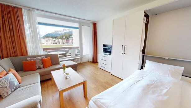 A hotel room with a sofa, a bed, a TV, a wardrobe, and a balcony with a mountain view. - Well-kept holiday apartament house in a prime location in St. (St. Moritz)