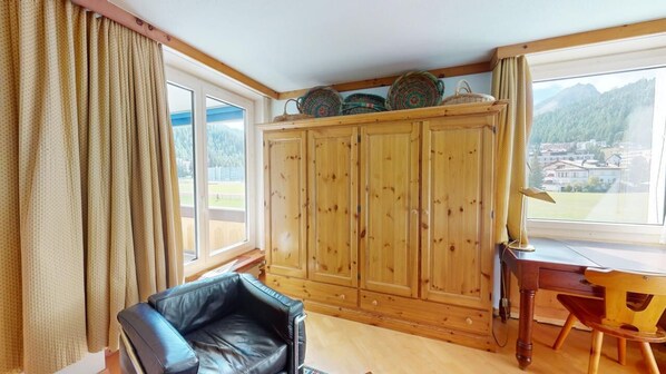 A room with a wooden cabinet, a black leather chair, a wooden desk, and a view of a village through large windows. - Well-kept holiday apartament house in a prime location in St. (St. Moritz)
