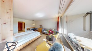 A modern hotel room with a wooden floor, a bed, a sofa, a dining table, and a balcony with a view. - Well-kept holiday apartament house in a prime location in St. (St. Moritz)