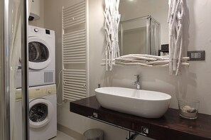 A bathroom with a washing machine, a sink, and a mirror.
