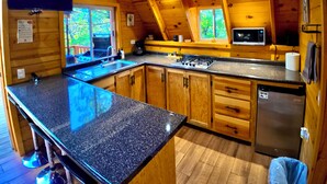 Une cabane en bois dotée d’une cuisine avec des comptoirs en granit, des armoires en bois, un lave-vaisselle et un four à micro-ondes.