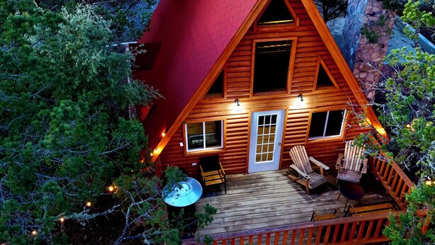 Une cabane en bois avec un toit rouge, une terrasse avec des chaises et un mur en pierre.