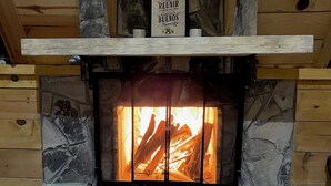 Une cheminée en pierre, surmontée d’une enseigne, et flanquée de deux fauteuils.