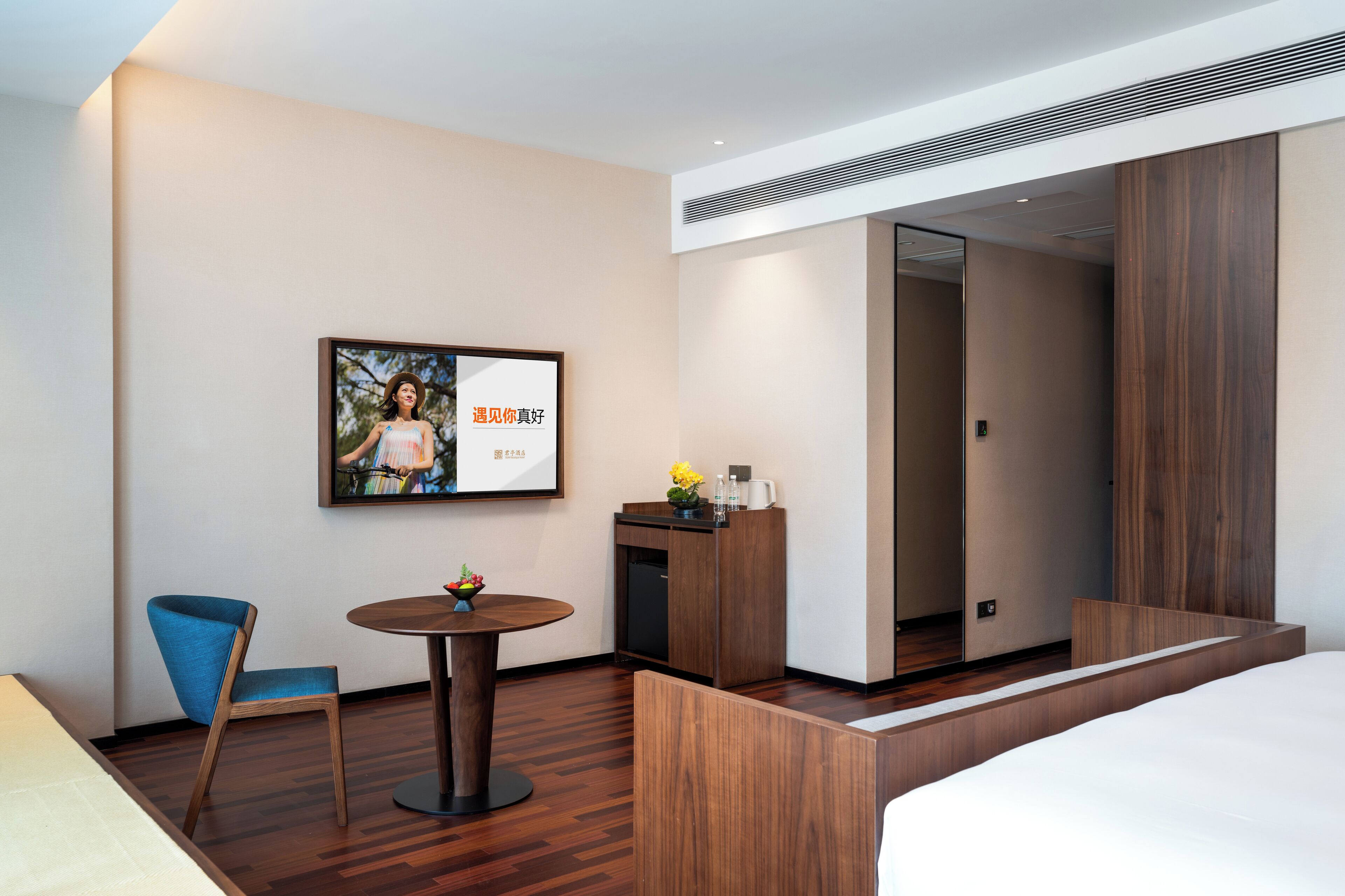 A hotel room with a bed, a desk with a vase of flowers, a chair, a small round table, and a framed picture on the wall.