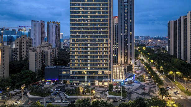 Un hotel moderno con un llamativo letrero 'C+', rodeado de rascacielos y una concurrida calle urbana.