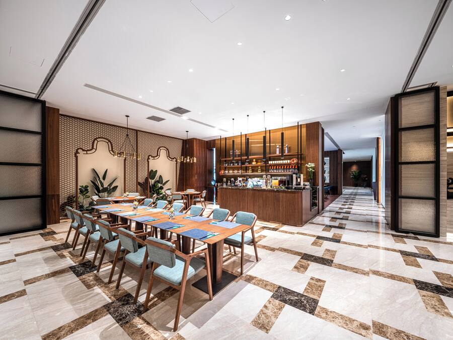 Un moderno vestíbulo de hotel con una larga recepción, zona de estar con mesas y sillas, y un suelo con diseño.