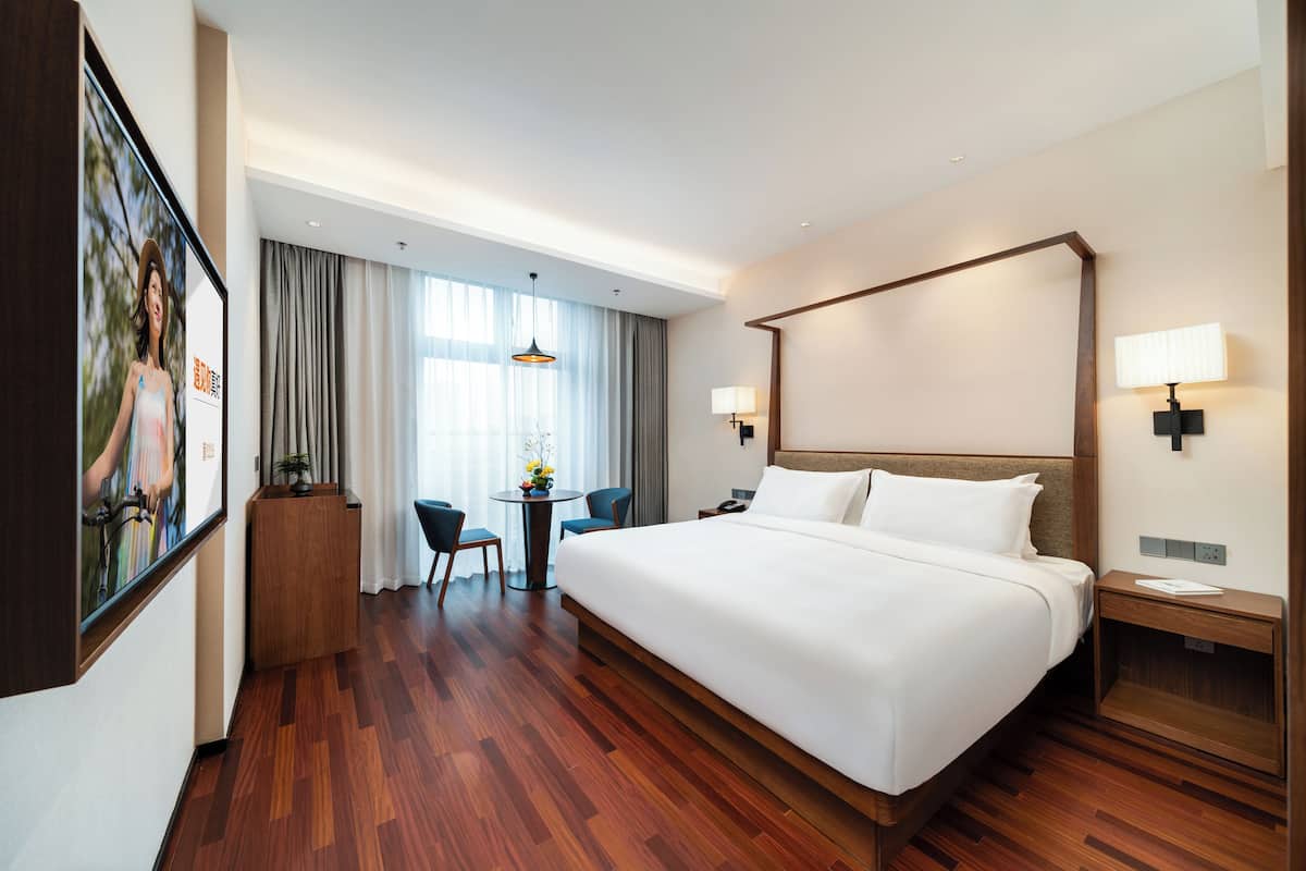 A hotel room with a large bed, a desk, chairs, and a view of the outdoors.