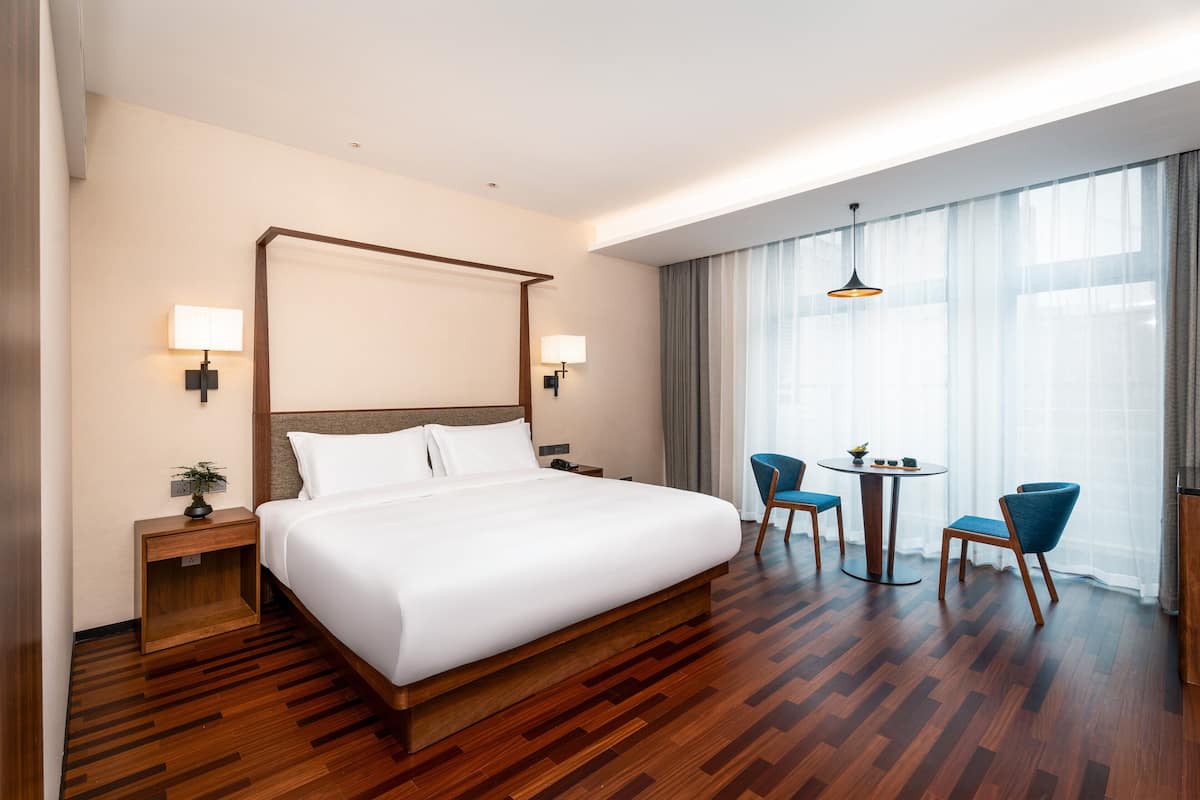 A hotel room with a large bed, two bedside tables, a small table with chairs, and a window with curtains.