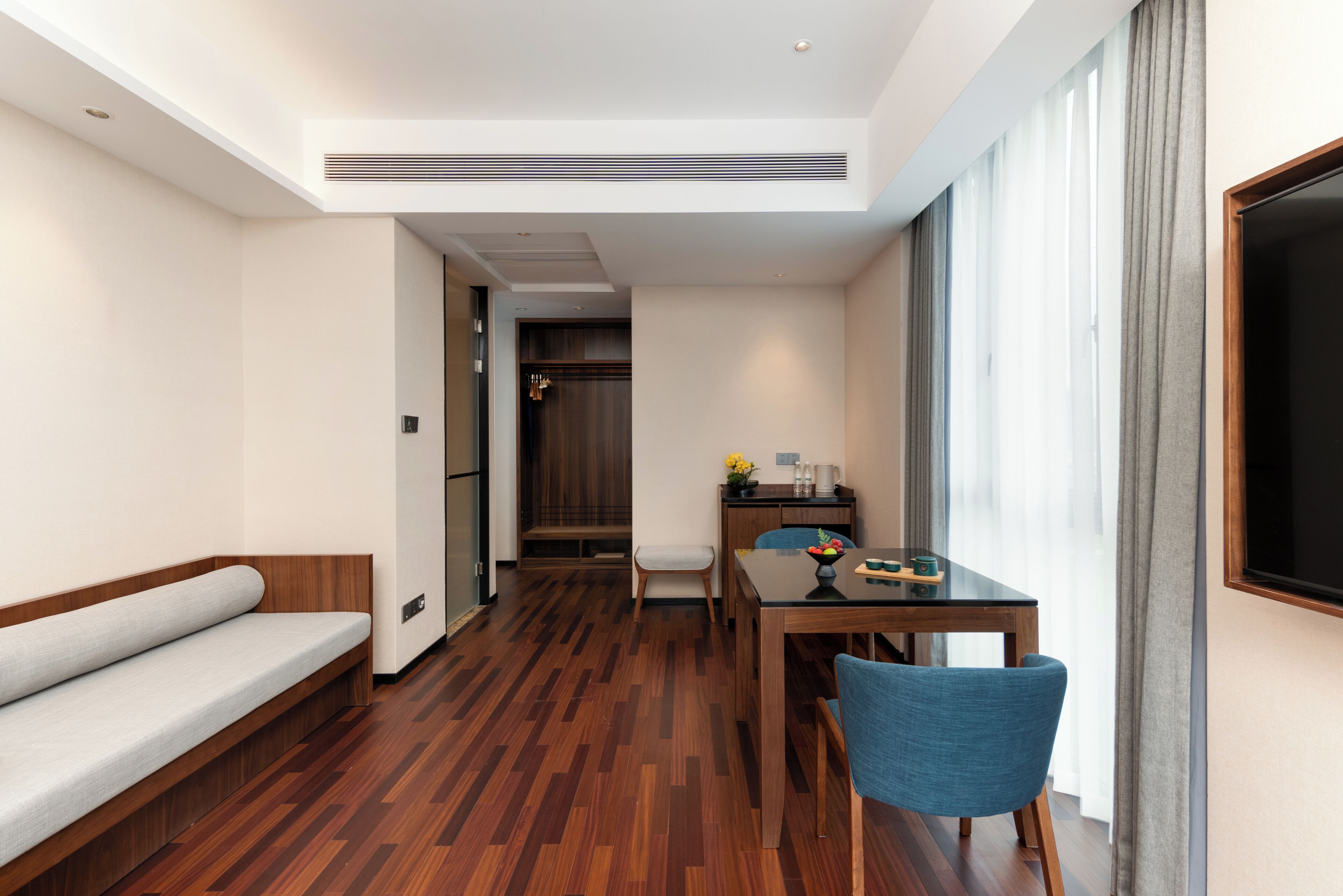 Ein modernes Hotelzimmer mit Holzboden, einer Couch, einem Esstisch mit Stühlen und einem großen Fenster mit Vorhängen.