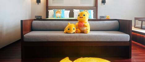 A hotel room with a grey sofa, two plush toys on it, and a large decorative rug on the floor.