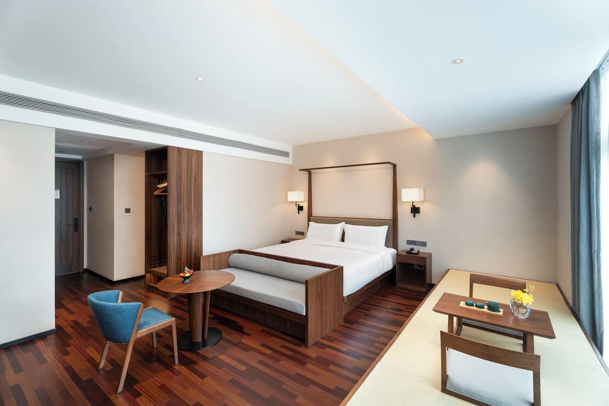 A modern hotel room with a bed, bedside tables, a small dining table, and a chair.