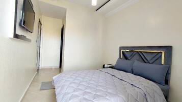 Un dormitorio con cama, televisor montado en la pared y puerta que da a otra habitación.