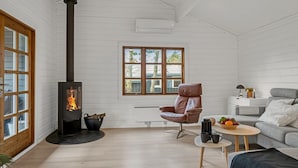 Une pièce chaleureuse avec un poêle à bois, un fauteuil en cuir confortable, un canapé et une petite table sur laquelle se trouve un panier de fruits.