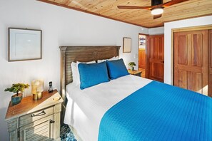 A bedroom with a wooden headboard, a bed with blue bedding, a bedside table with a lamp, and a nightstand with a plant. - Shoney Bear Cabin By Destination Big Bear: Pet Friendly! Hot Tub! Located Near Marinas & Lake! Air Hockey! Beautiful Outdoor Patio w/ Gazebo + Built In Gas BBQ and Grill! (Big Bear Lake)