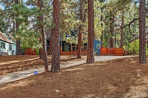 A residential area with a house surrounded by tall pine trees, a paved driveway, and a blue sign with 'ADT' on it. - Shoney Bear Cabin By Destination Big Bear: Pet Friendly! Hot Tub! Located Near Marinas & Lake! Air Hockey! Beautiful Outdoor Patio w/ Gazebo + Built In Gas BBQ and Grill! (Big Bear Lake)