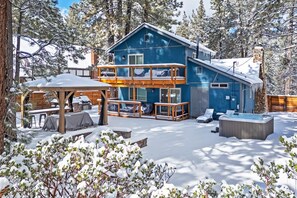 A two-story cabin with a balcony, a hot tub, and a covered outdoor seating area.