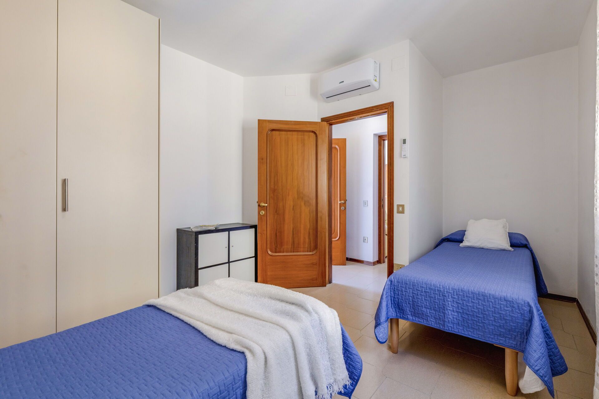 A bedroom with two beds, a wardrobe, a small cabinet, and an air conditioning unit.