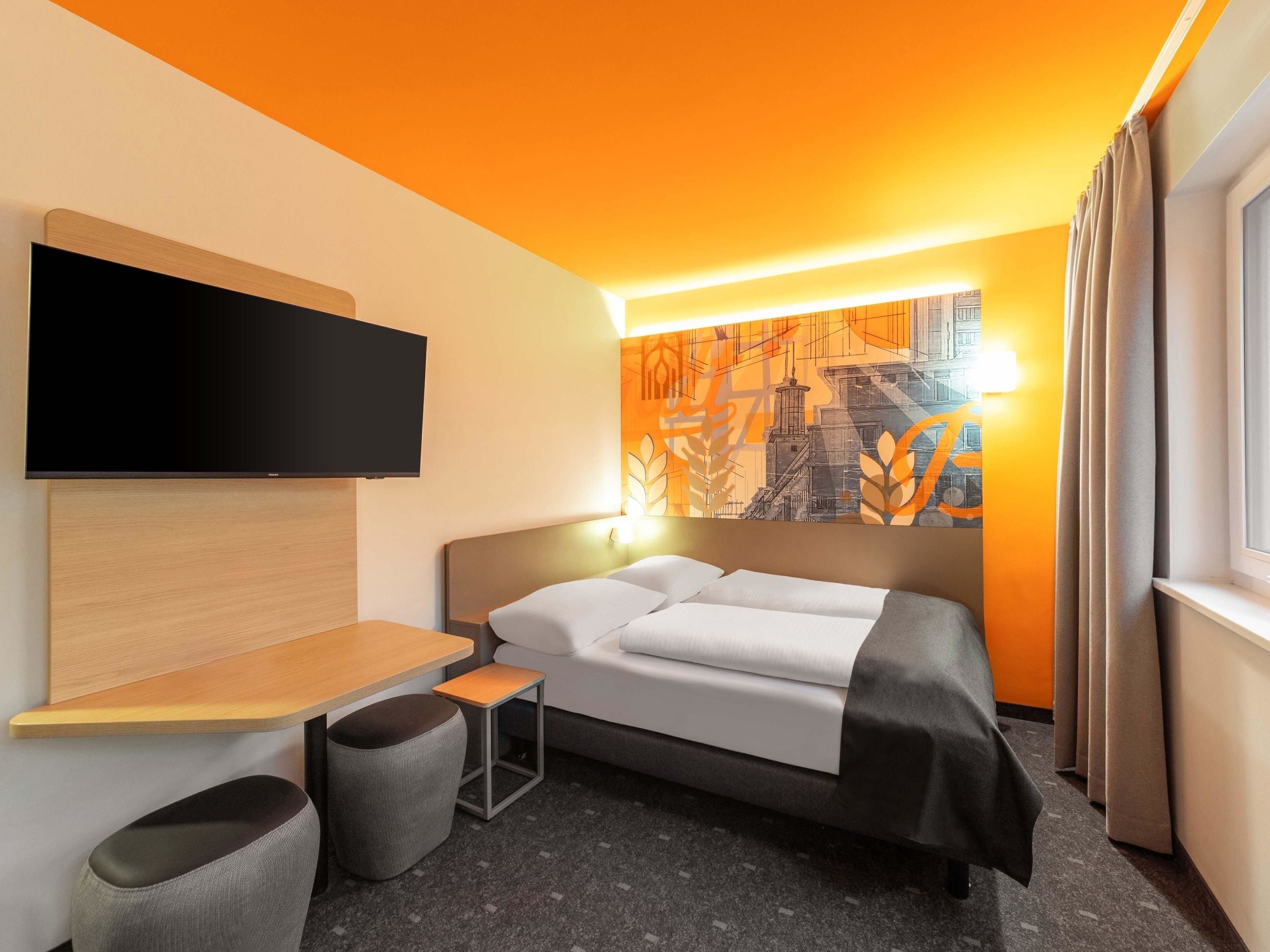 Una habitación de hotel moderna con una cama, un televisor de pantalla plana, una mesita y una silla.