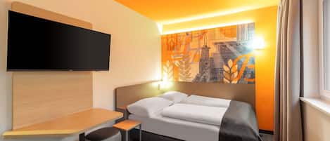 A modern hotel room with a bed, a flat-screen TV, a small table, and a chair.