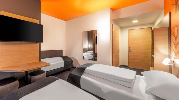 A modern hotel room with a large bed, a desk, and a mirror. - B&B HOTEL Hagen (Hagen)