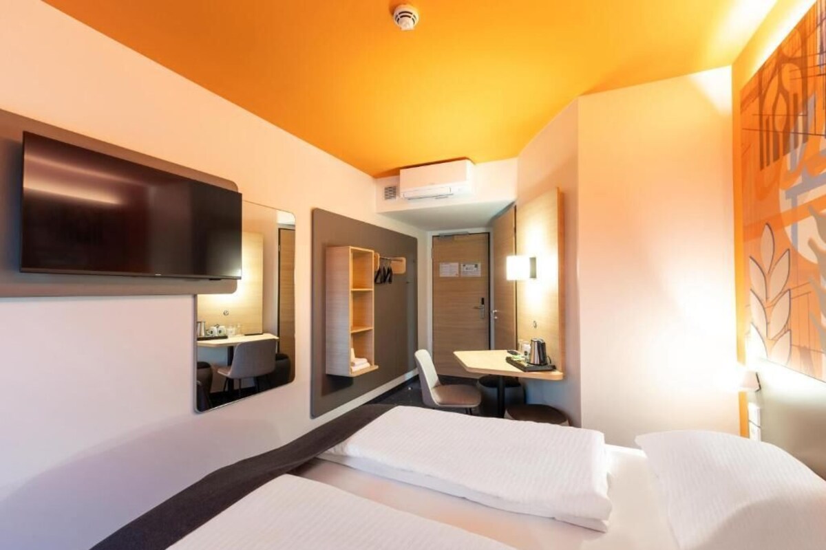 A hotel room with two beds, a desk, a chair, a TV, and a mirror.