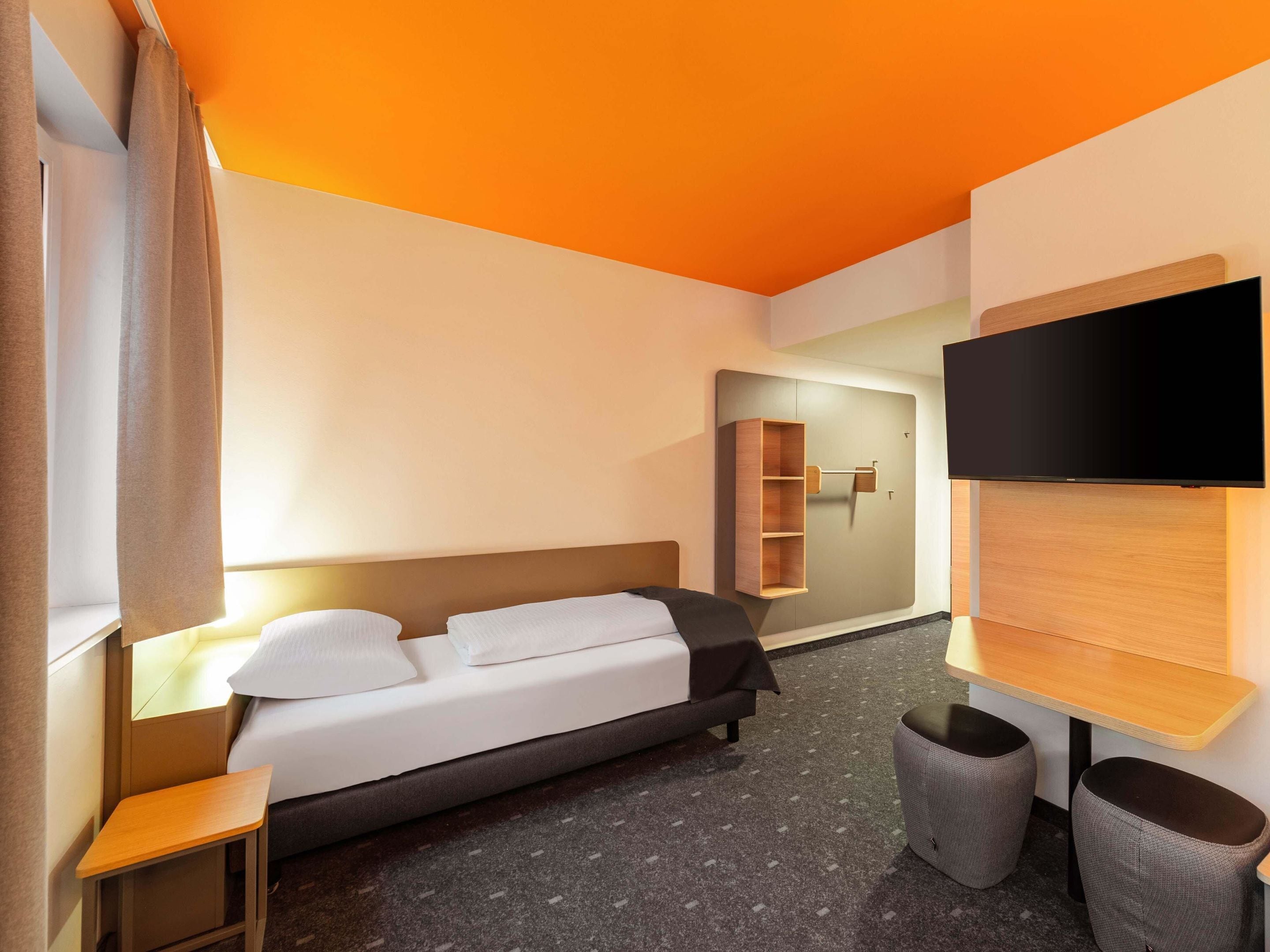 Ein modernes Hotelzimmer mit Bett, Nachttisch, Fernseher und einer kleinen Sitzecke.