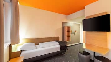 Una habitación de hotel moderna con una cama, mesita de noche, televisor y un pequeño rincón de descanso.